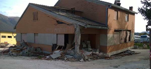 Un edificio pesantemente danneggiato dal sisma nel centro di Norcia. In alto la tendopoli allestita dalla Protezione Civile